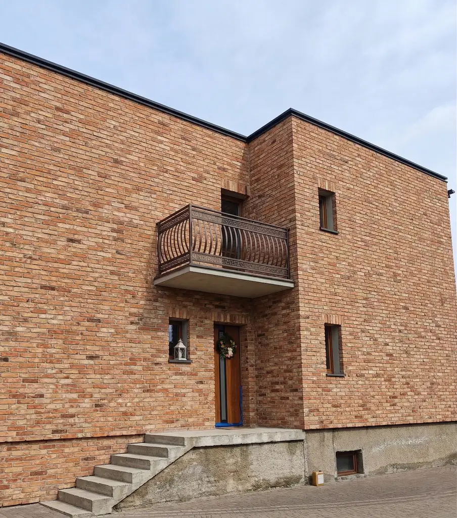 Efektowna elewacja starego domu po remoncie, pokryta historyczną cegłą.