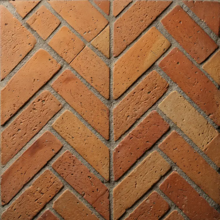 Zbliżenie na fragment podłogi ułożonej ze starych cegieł ułożonych w jodełkę. Widoczna szara fuga i naturalna faktura wyczyszczonej gliny.